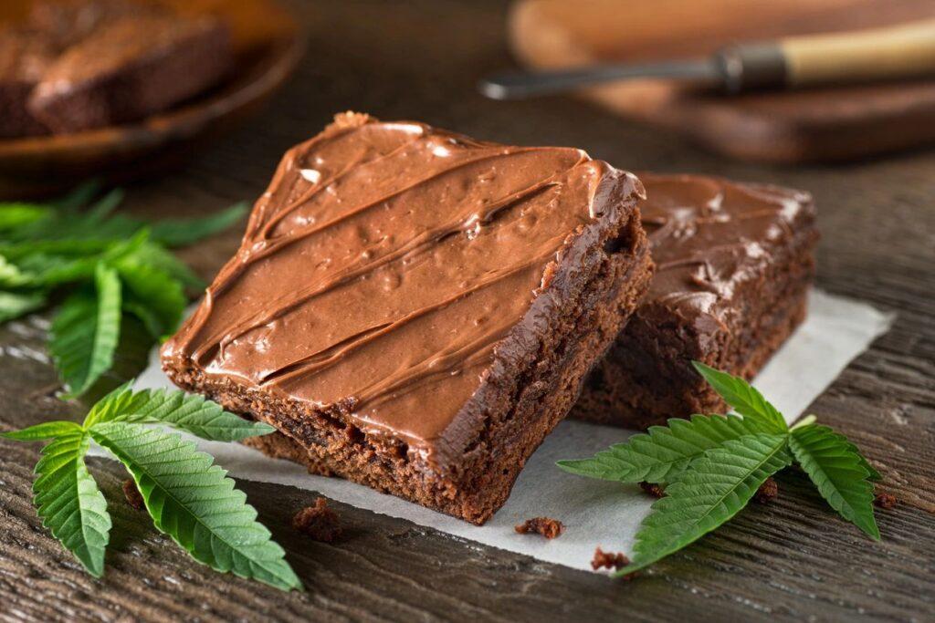beginners guide to making edibles course - a chocolate frost brownie on a plate with cannabis leaves around them.