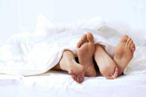 two sets of feet poking out from the covers - infused intimacy oil