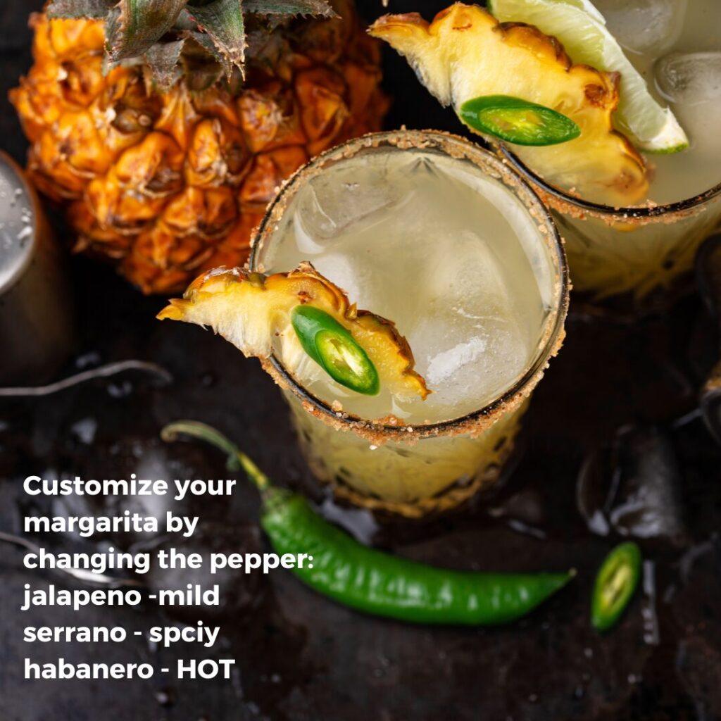 image from top view of spicy pineapple margaritas with a chile lime rim, garnish of slice of serrano pepper, slice of pineapple in a high ball glass