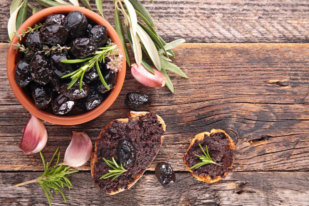 bowl of olives next to 2 slices of baguette spread with cannabis infused olive tapenade